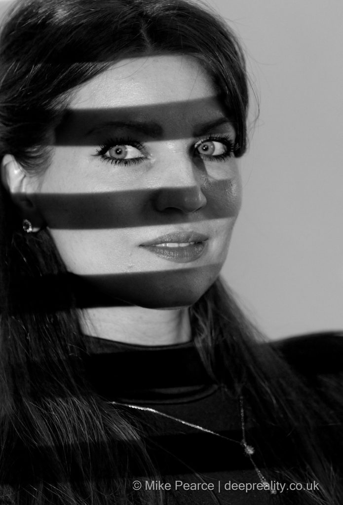 Black & white portrait shot of a woman with bands of light across her face.